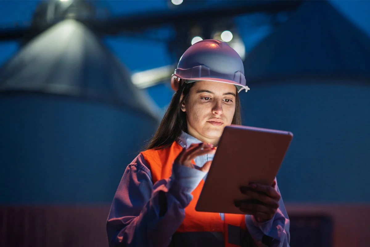 Woman in high vis and hard hat looking at tablet in the dark