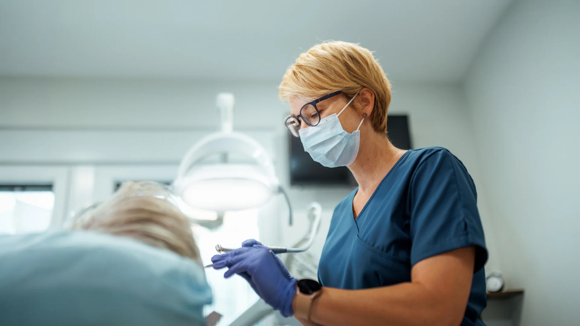 Dentist in glasses using tools on a patient