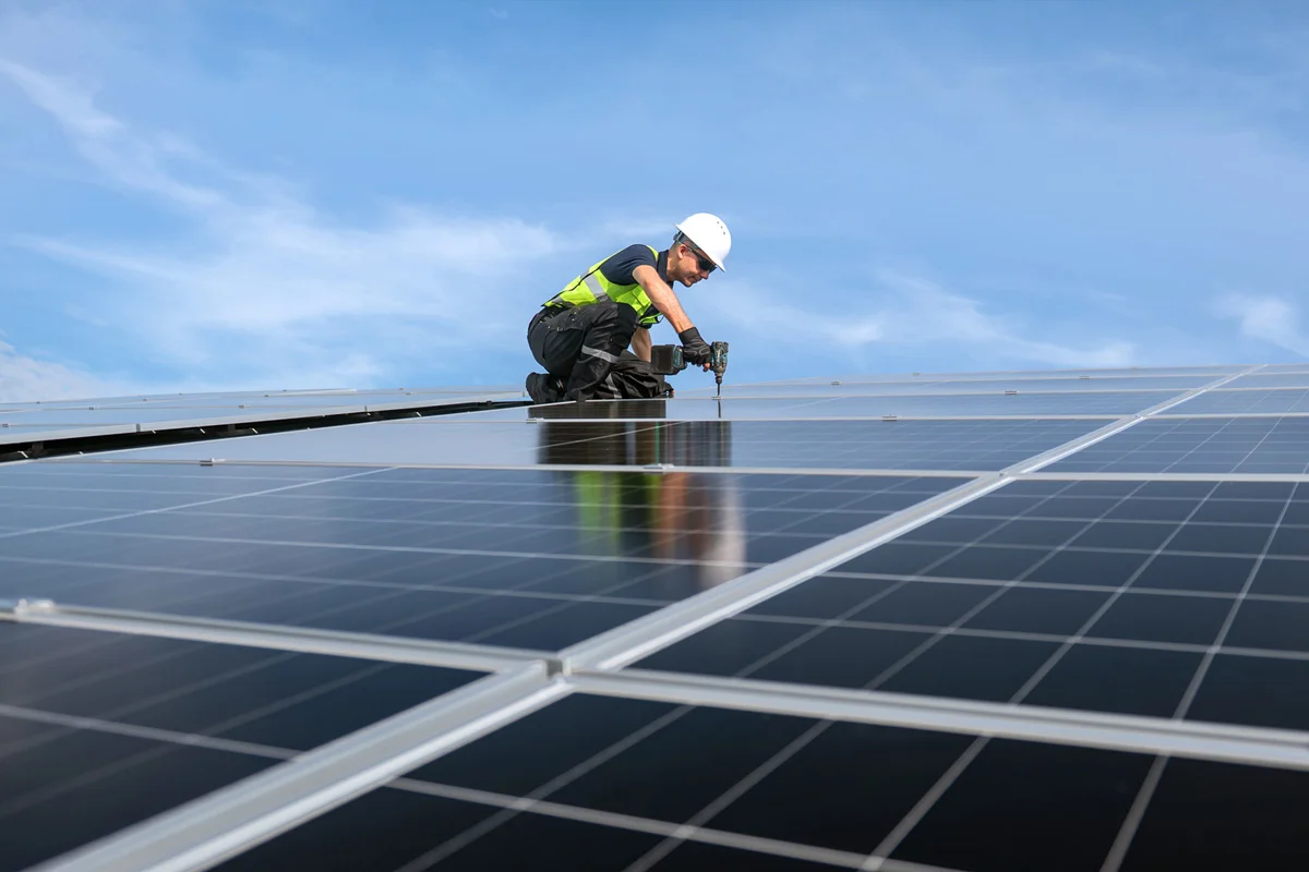 Man in hight vis and hard hat drilling solar panels